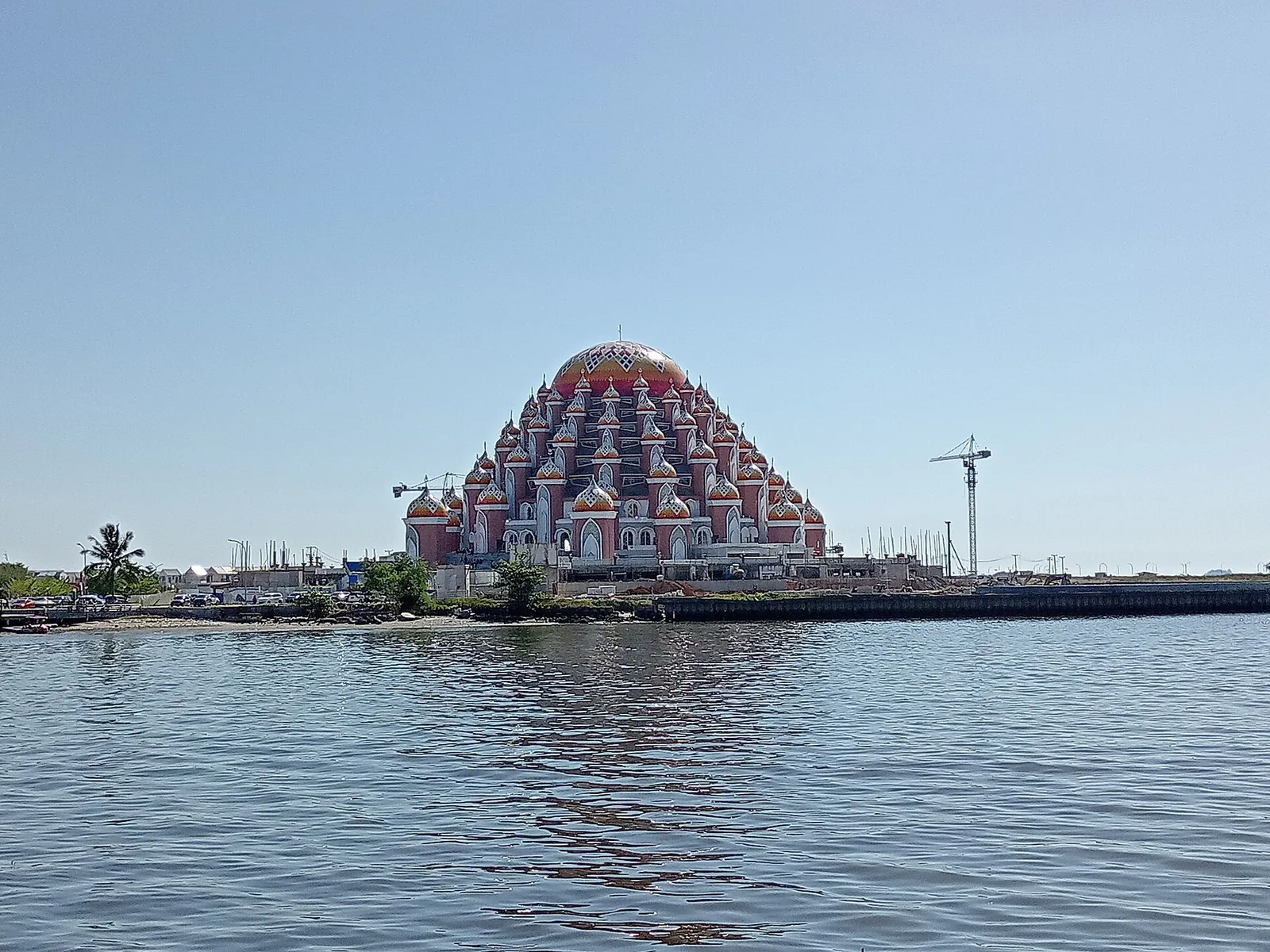 A mosque with many red, orange and blue domes beside the water on the Makassar seafront