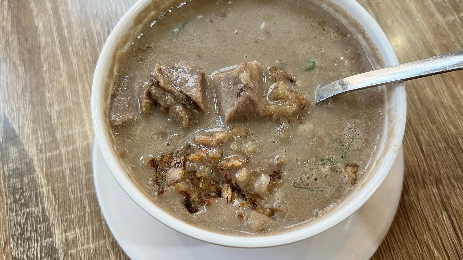A bowl of coto Makassar, dark beef soup with chunks of meat and fried shallots