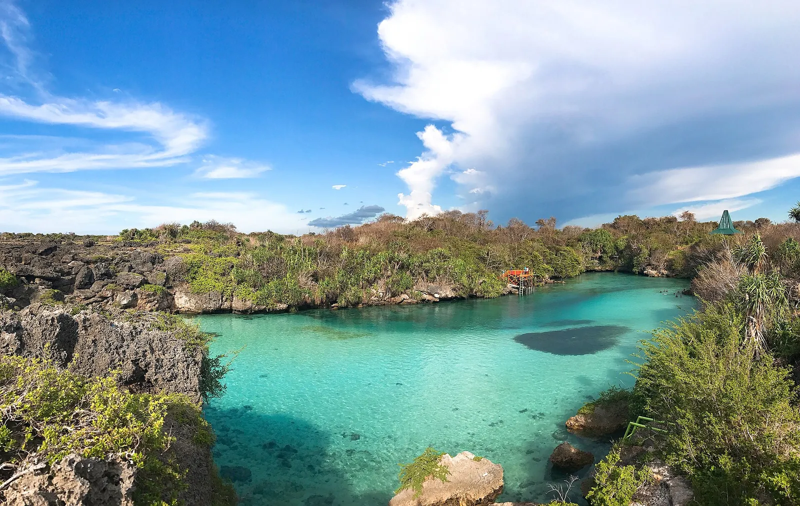 Turquoise saltwater lagoon of Weekuri surrounded by grey coral rock and green shrubs
