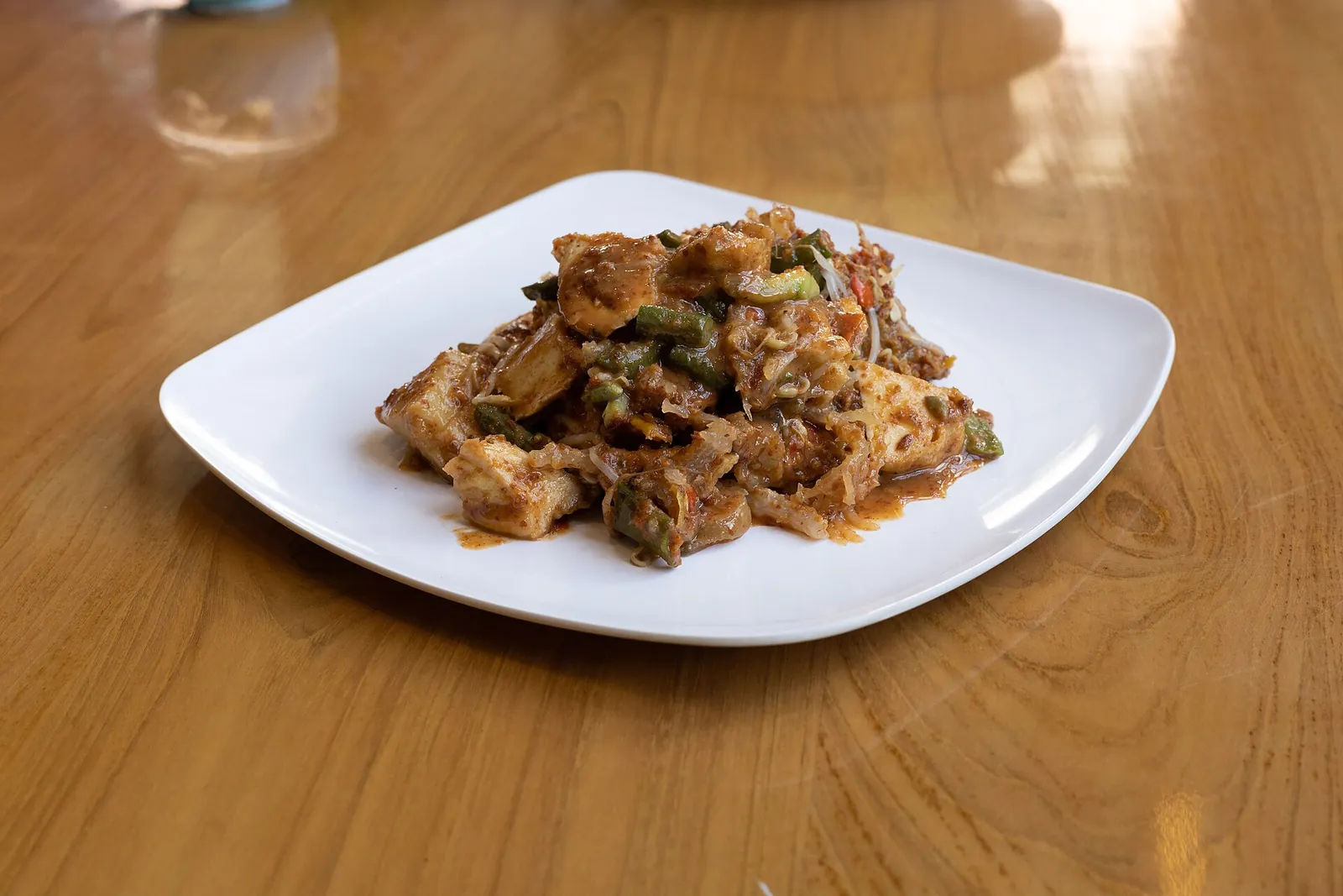 A plate of rujak cingur with vegetables, tofu and sliced beef snout in a dark peanut and petis sauce