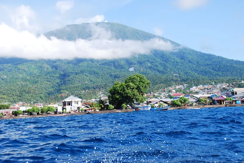 The cone of Mount Gamalama rising above Ternate's waterfront houses, seen from the sea
