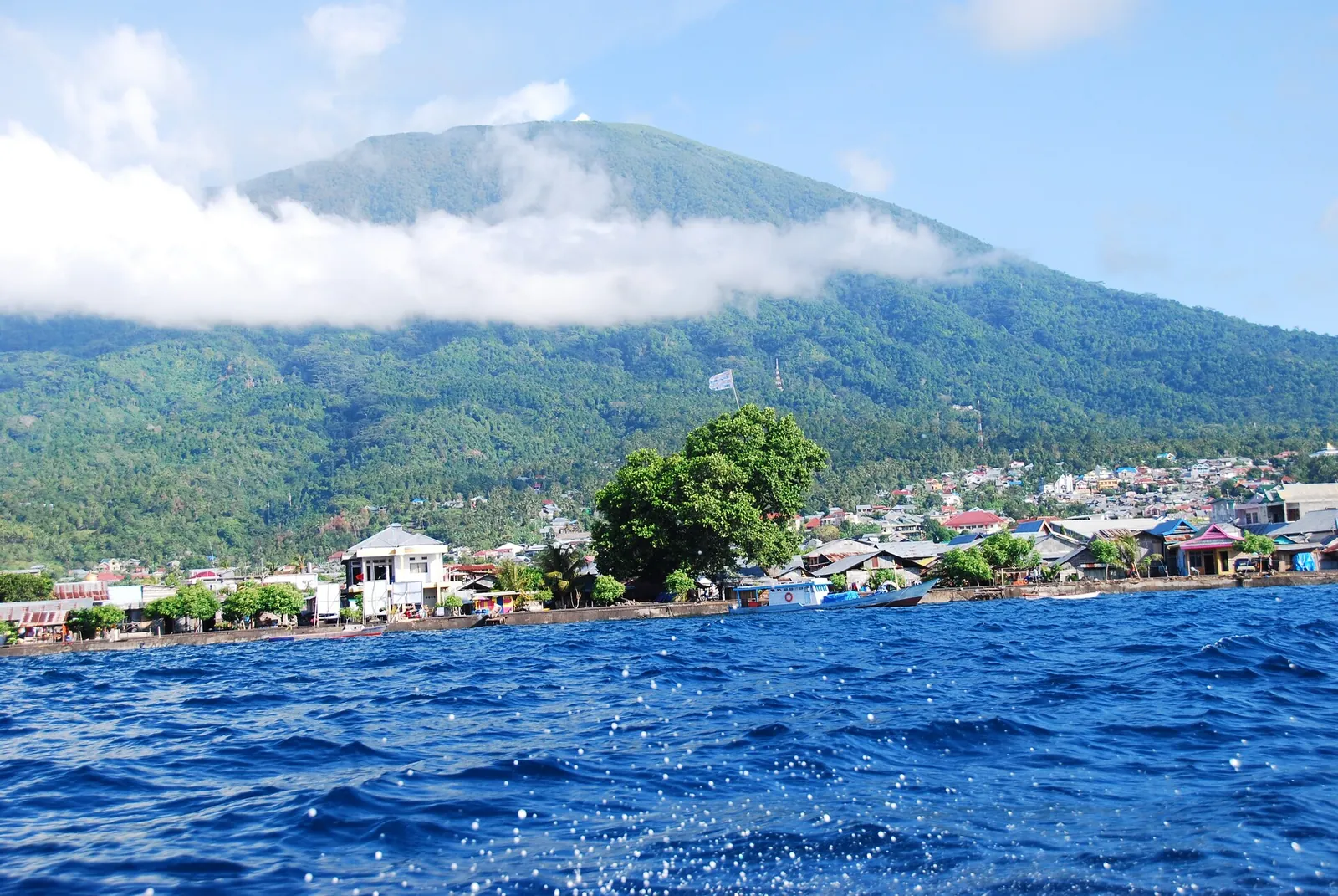 The cone of Mount Gamalama rising above Ternate's waterfront houses, seen from the sea