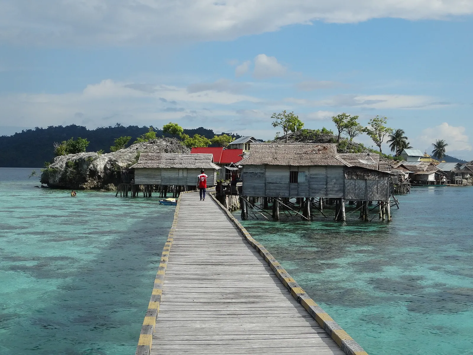 Wooden boardwalk leading over turquoise shallows to stilt houses of the Bajau village of Kabalutan in the Togean Islands