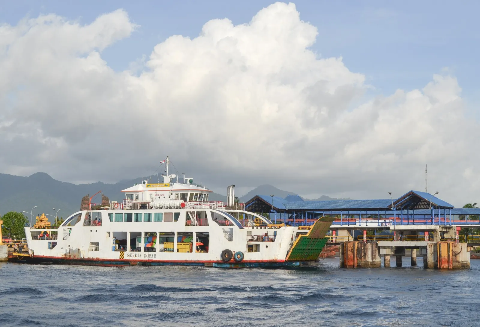 White car ferry moored at a harbour pier under a blue sky with large white clouds