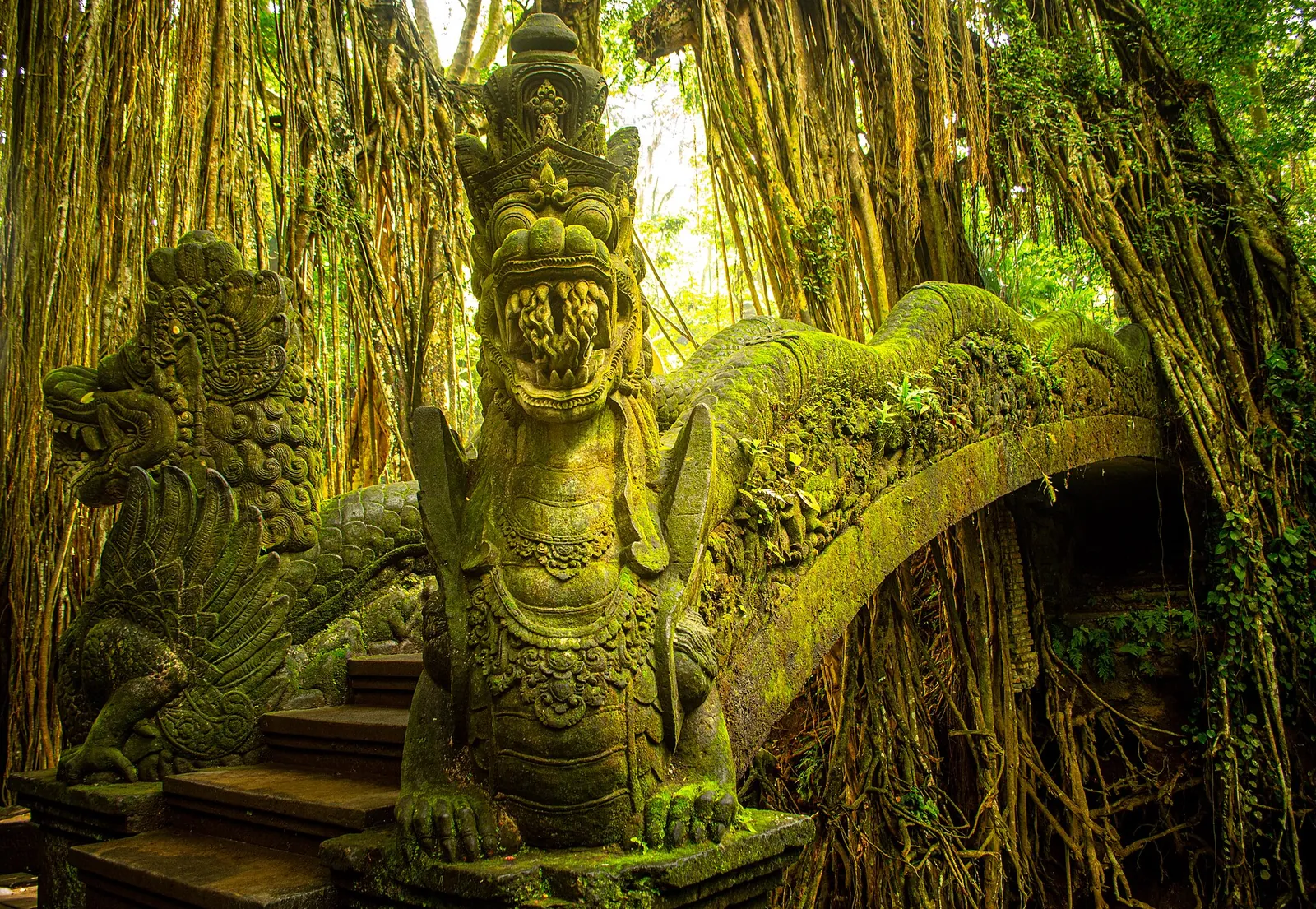 Moss-covered stone dragon bridge under banyan roots in the Ubud Monkey Forest