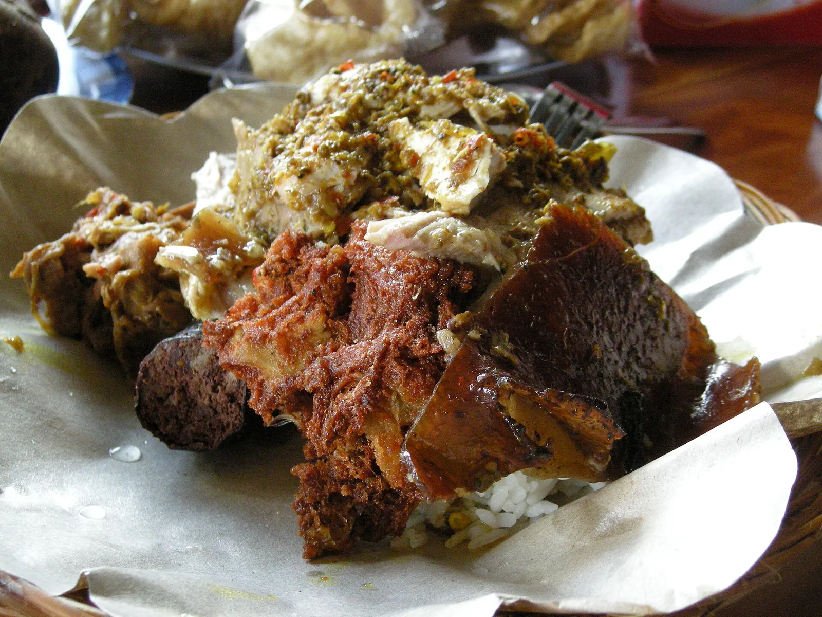 Plate of babi guling with crackling, roast pork, lawar and rice on paper