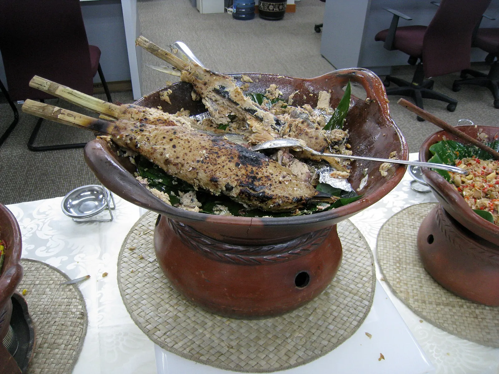 Grilled sate bandeng milkfish skewers on bamboo sticks in a clay serving bowl at a buffet