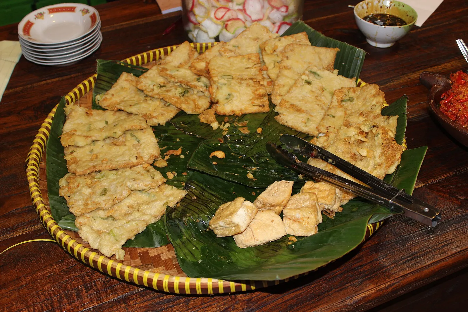 A large woven tray of fried tempeh and fried tofu pieces on banana leaves