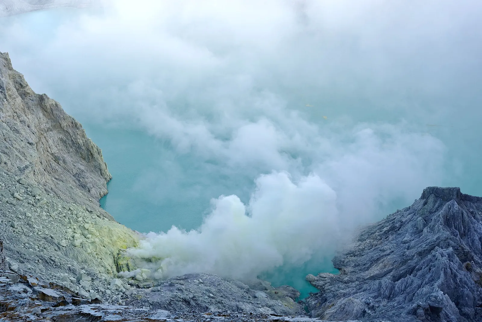 Turquoise acid lake inside the crater of Kawah Ijen, East Java, with sulphur steam drifting over the water