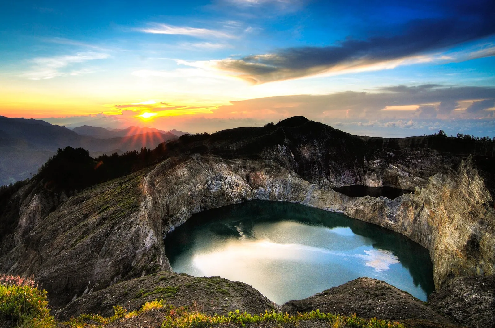 Sunrise over one of the Kelimutu crater lakes on Flores, its water reflecting the sky inside a steep crater