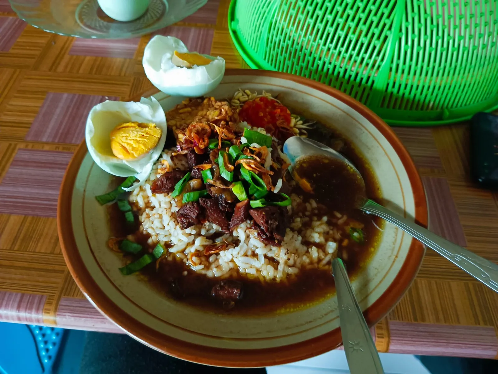 A plate of nasi rawon, rice with dark beef soup, crisp shallots, spring onion and a halved salted egg