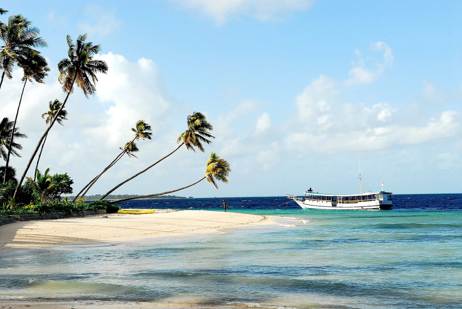 White sand spit with palm trees and a boat moored offshore in Wakatobi
