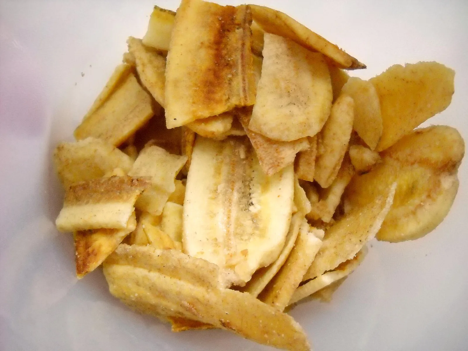 A pile of thin, golden banana chips on a white plate