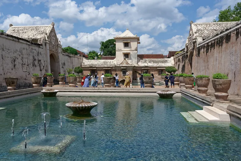 Turquoise bathing pools with fountains and a white tower at Taman Sari Water Castle in Yogyakarta under a blue sky