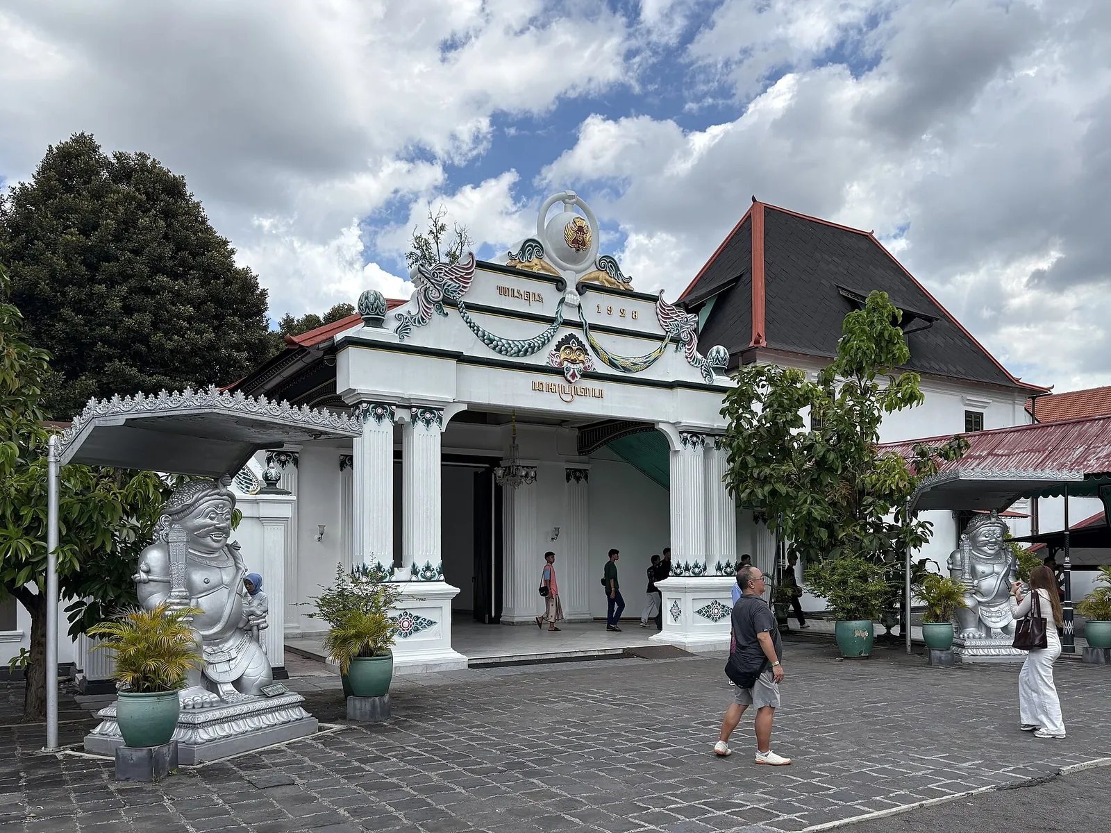 White Donopratono gate with guardian statues at the Kraton of Yogyakarta, with visitors in the courtyard