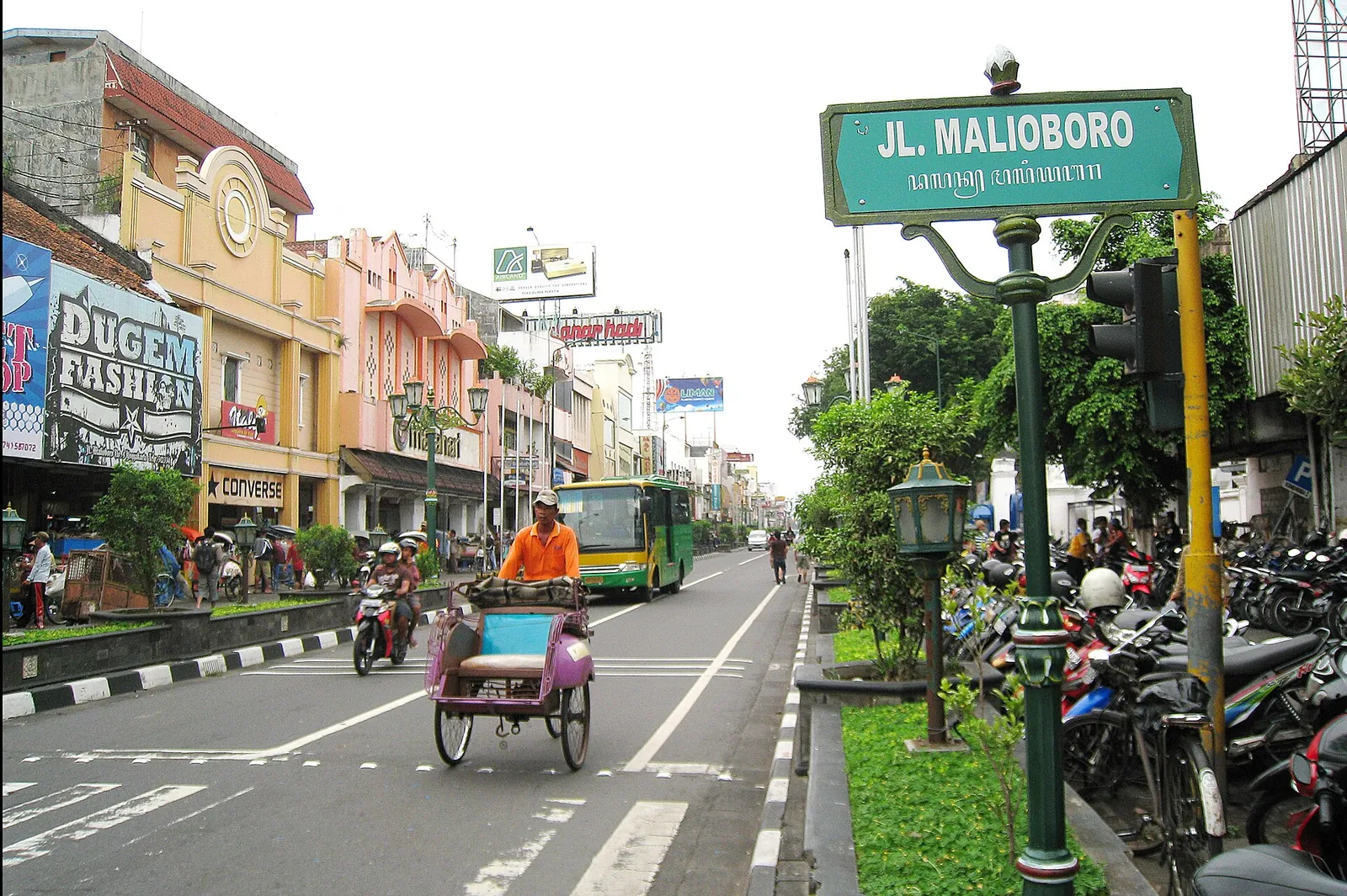 Jalan Malioboro in Yogyakarta with a street sign, a becak pedicab, shops and a TransJogja bus