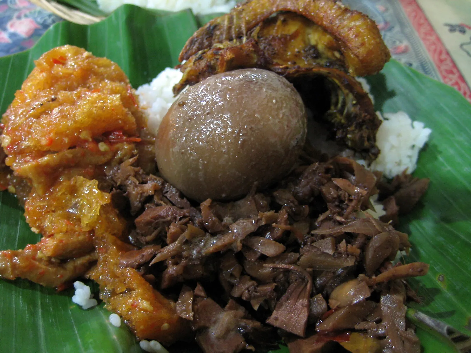Close-up of nasi gudeg with brown jackfruit stew, a spiced egg and chicken on a banana leaf