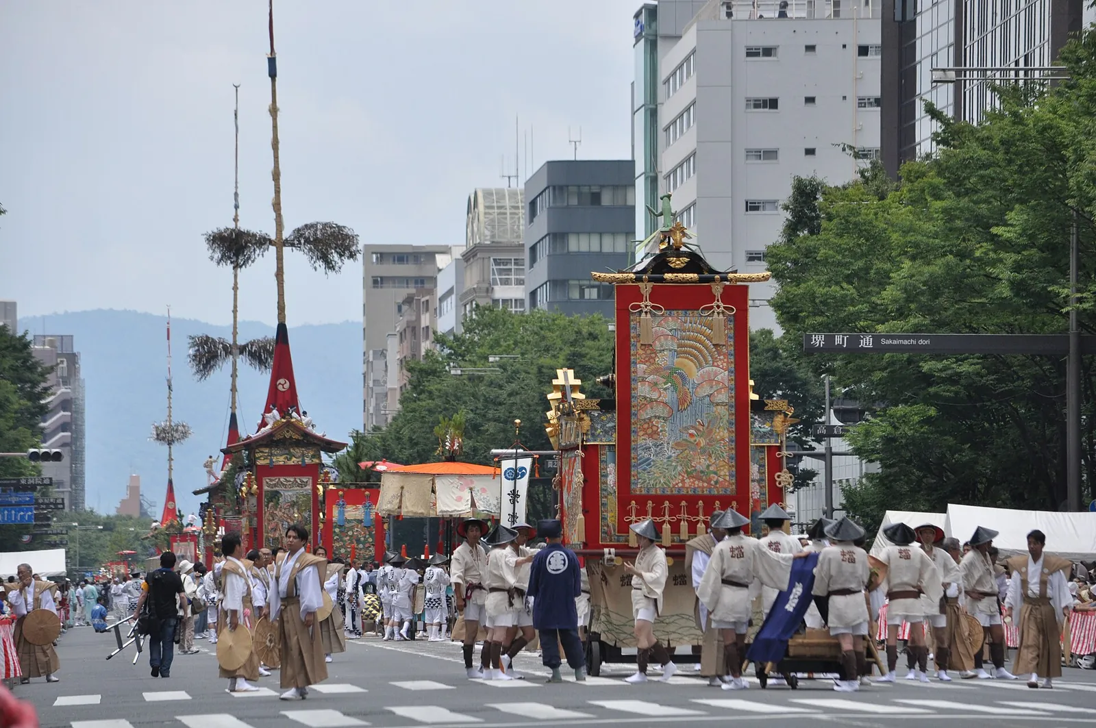Vysoké vozy Gion Matsuri tažené širokou kjótskou třídou skupinami v tradičních oděvech