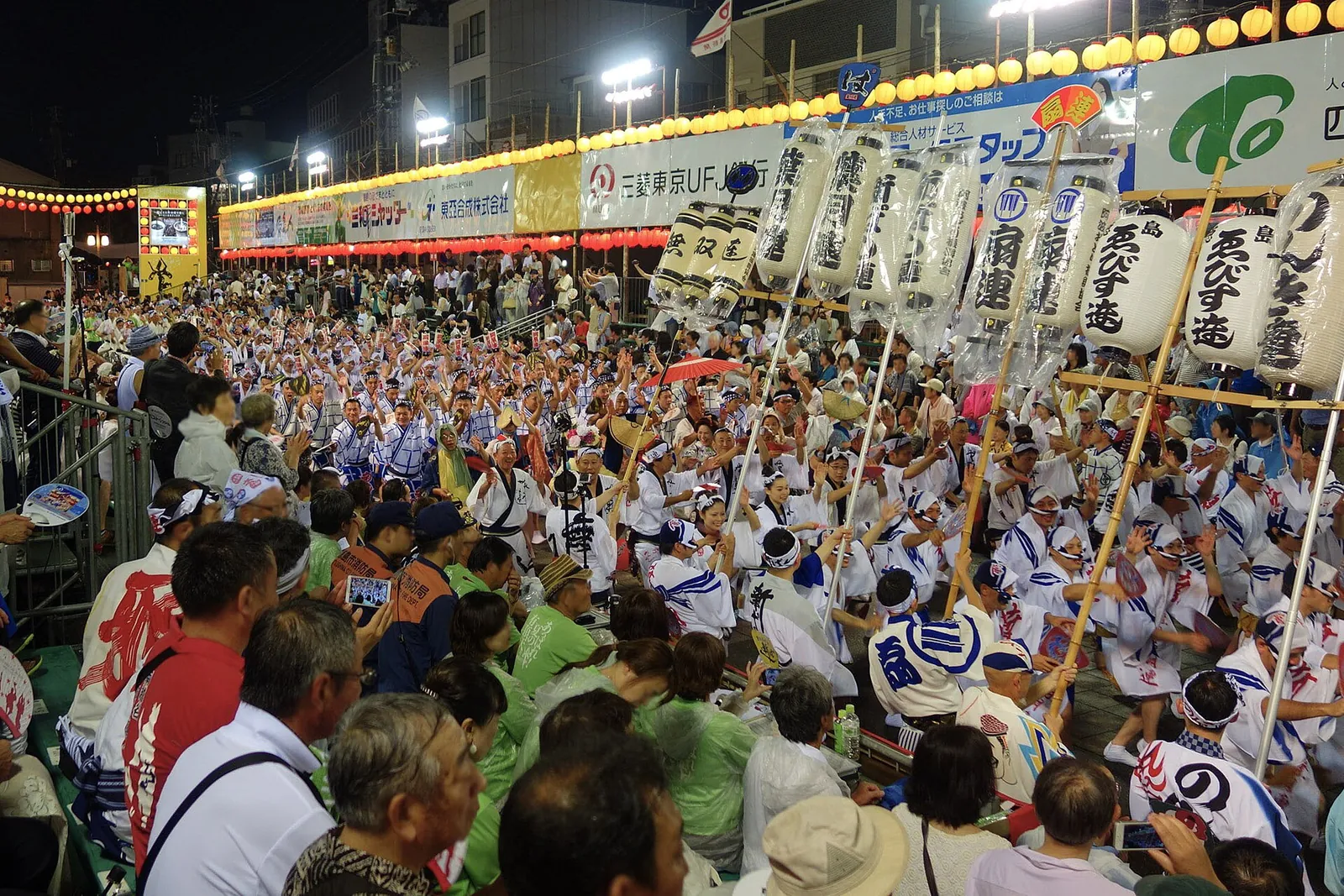 Diváci na tribunách sledující velkou skupinu tanečníků Awa Odori s lucernami v Tokushimě
