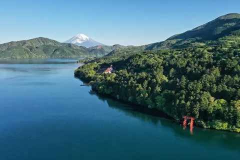 Jezero Ashi se rozprostírá směrem k zasněžené hoře Fuji, s červenou torii svatyně Hakone na zalesněném břehu