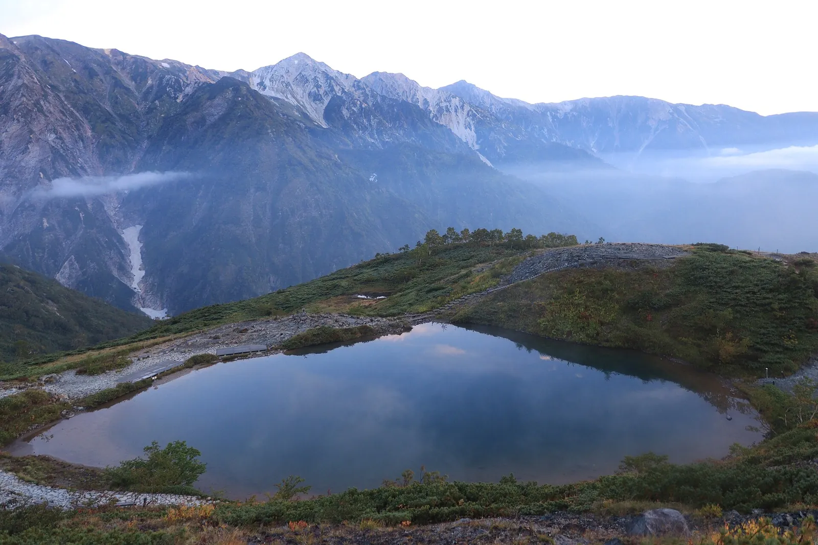 L'étang de Happo, sur la crête de Happo, reflétant le ciel, avec les sommets déchiquetés de Hakuba Sanzan derrière