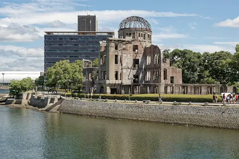 Zřícená Atomic Bomb Dome s holou ocelovou kopulí, pohled přes řeku Motoyasu pod modrou oblohou