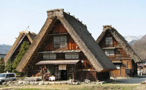 Velký statek gassho-zukuri se strmou střechou z došků v Ogimachi, Shirakawa-go, pod modrou oblohou, za ním kopce poprášené sněhem