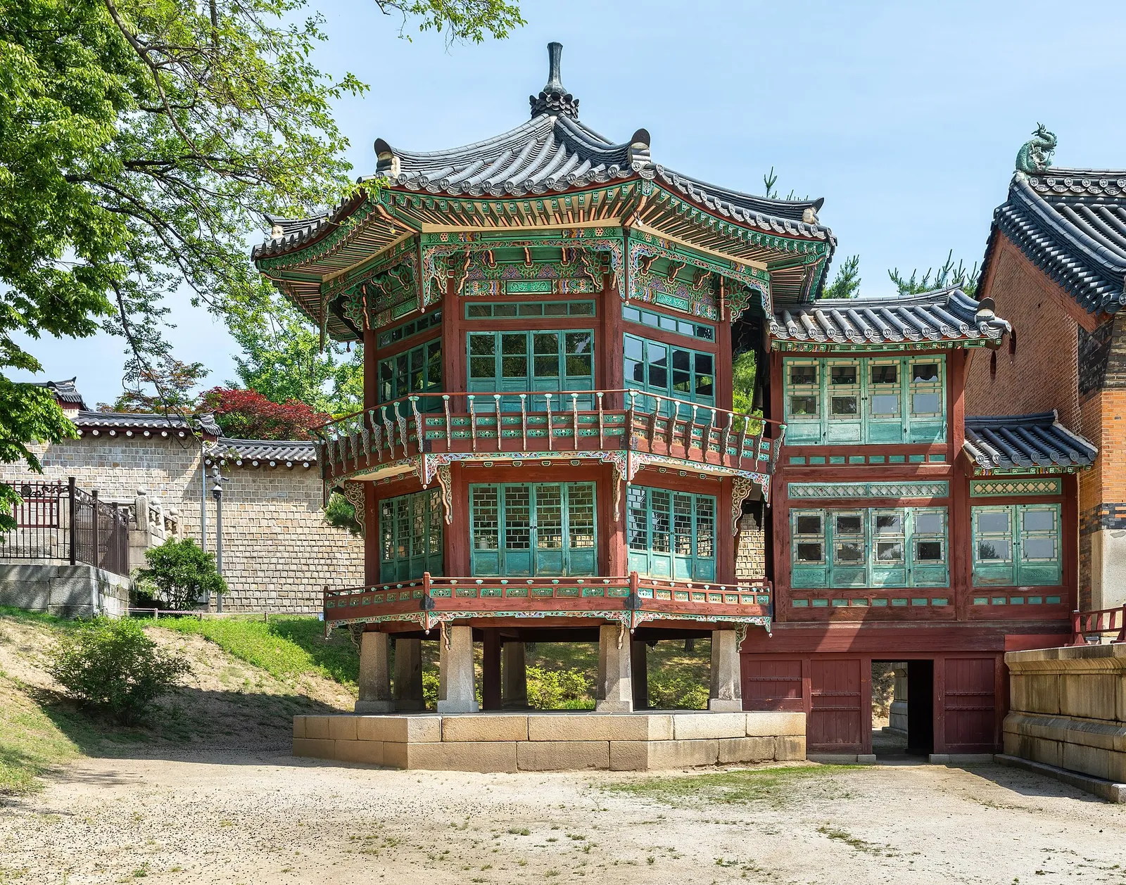 The two-storey painted tower of Jibokjae Hall at Gyeongbokgung under a blue sky, with spring trees