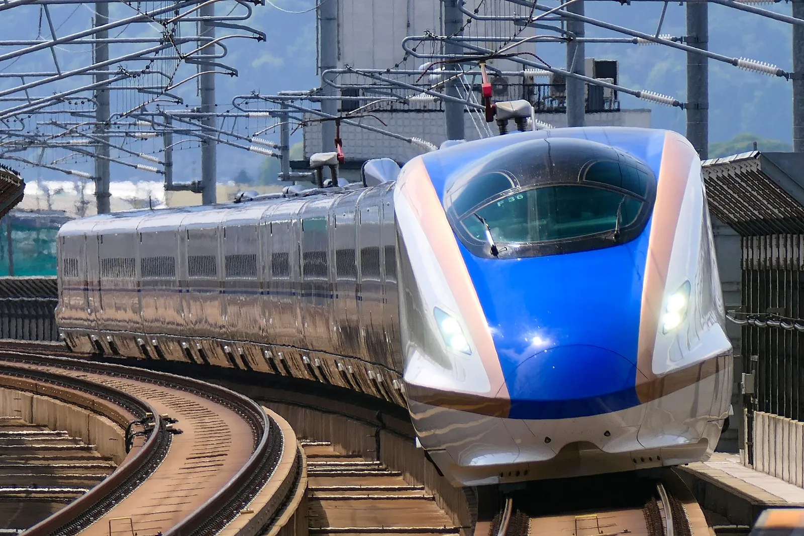 Modrobílý vlak Hakutaka řady E7 zatáčí do stanice Shin-Takaoka na šinkansenu Hokuriku