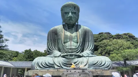 Bronzový Velký Buddha z Kamakury sedící pod širým nebem v Kotoku-in pod modrou oblohou, za ním zalesněné kopce