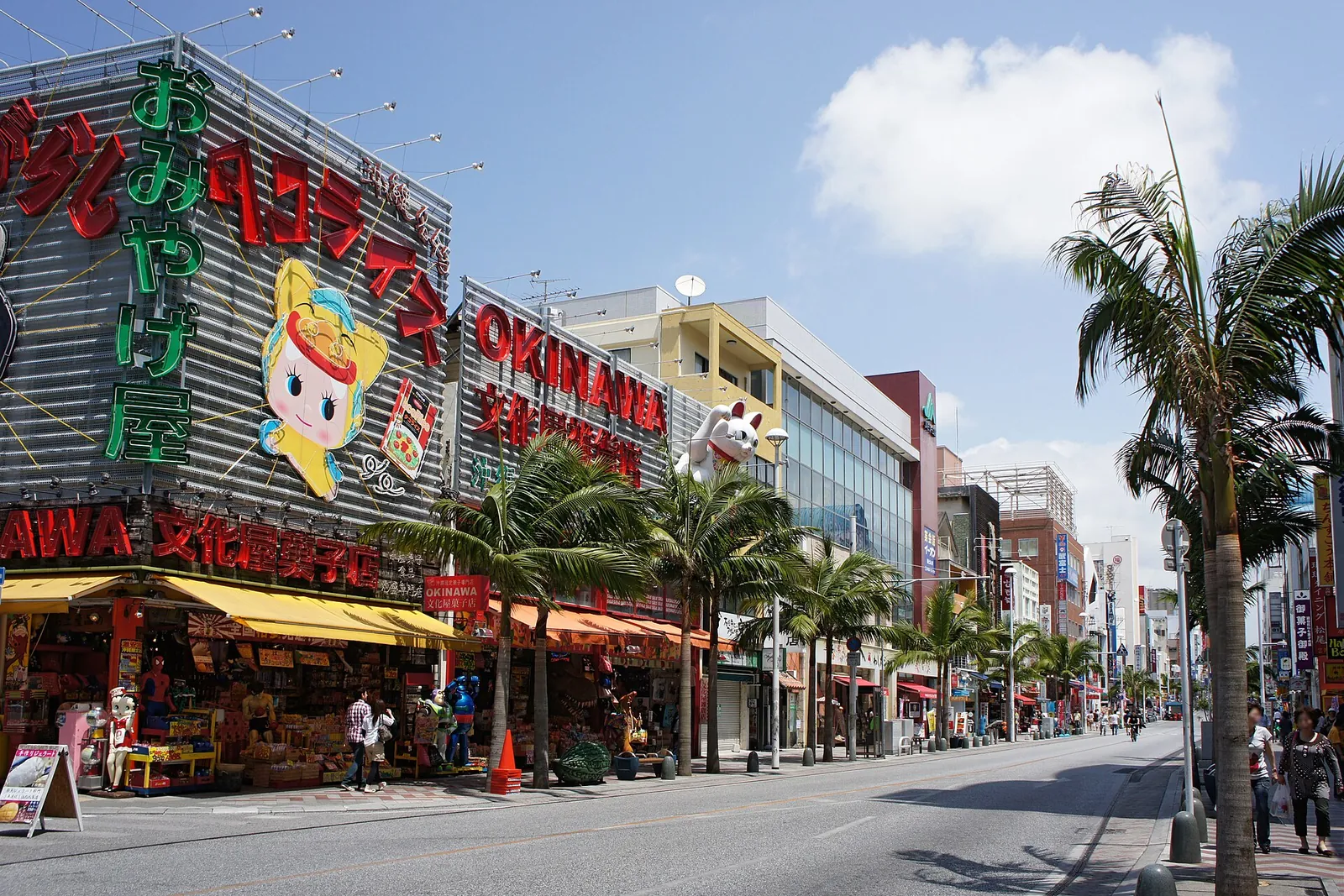 Kokusai-dori, en Naha, en un día soleado: una calle ancha bordeada de palmeras y letreros de tiendas