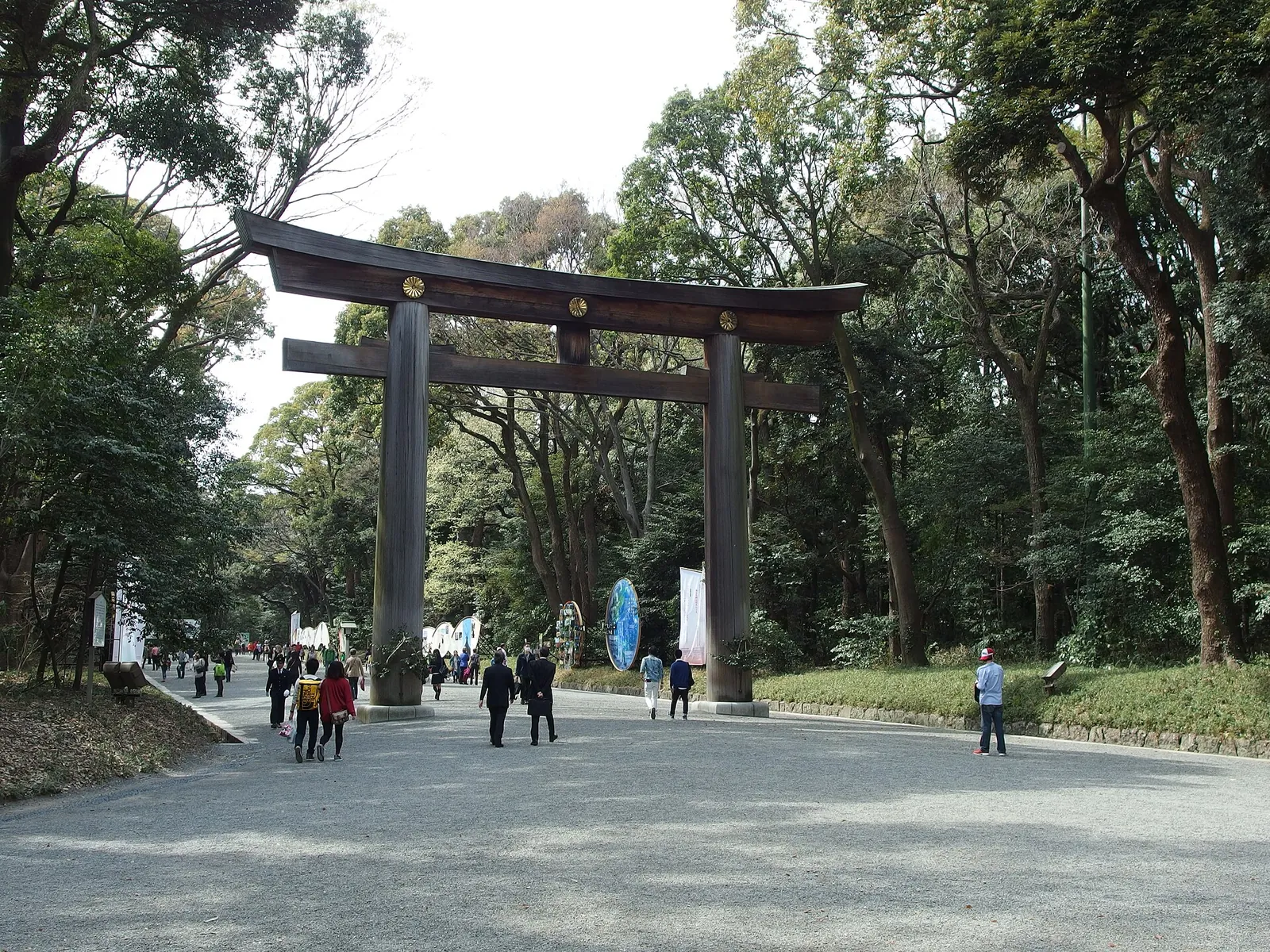 Velké dřevěné torii na široké štěrkové příchodové cestě k Meiji Jingu, orámované vysokými stromy