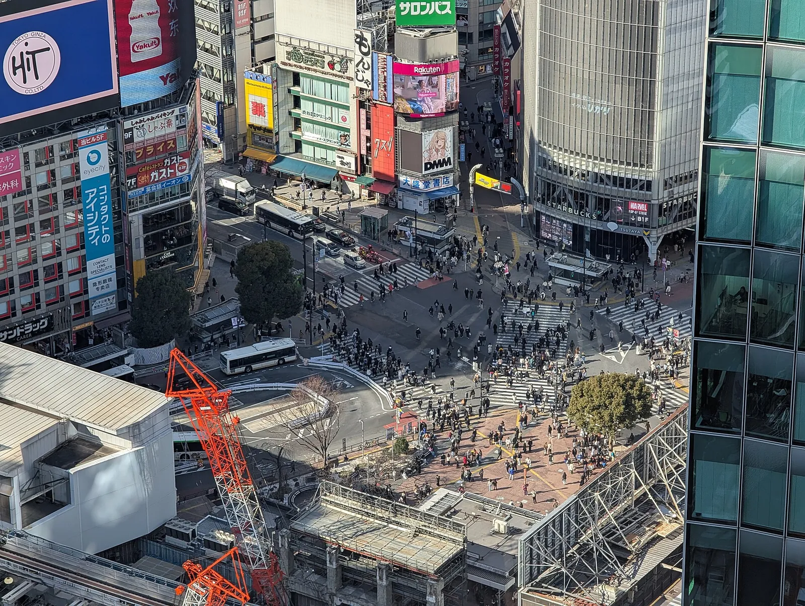 Davy proudící přes křižovatku Shibuya ze všech stran, viděné z velké výšky mezi billboardy a autobusy