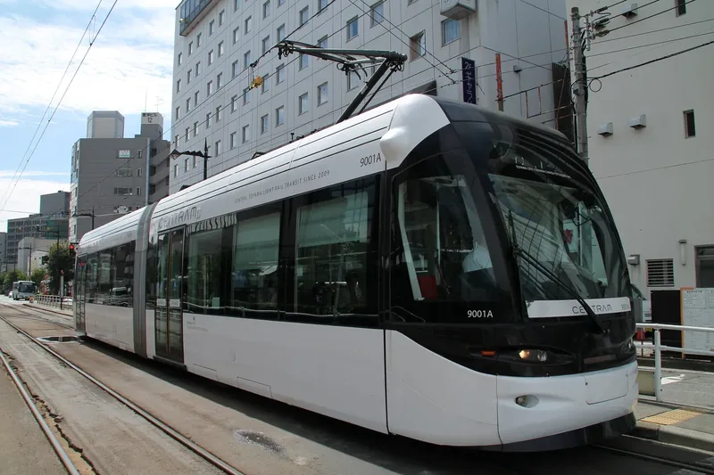 A modern tram travelling along a street in Toyama.