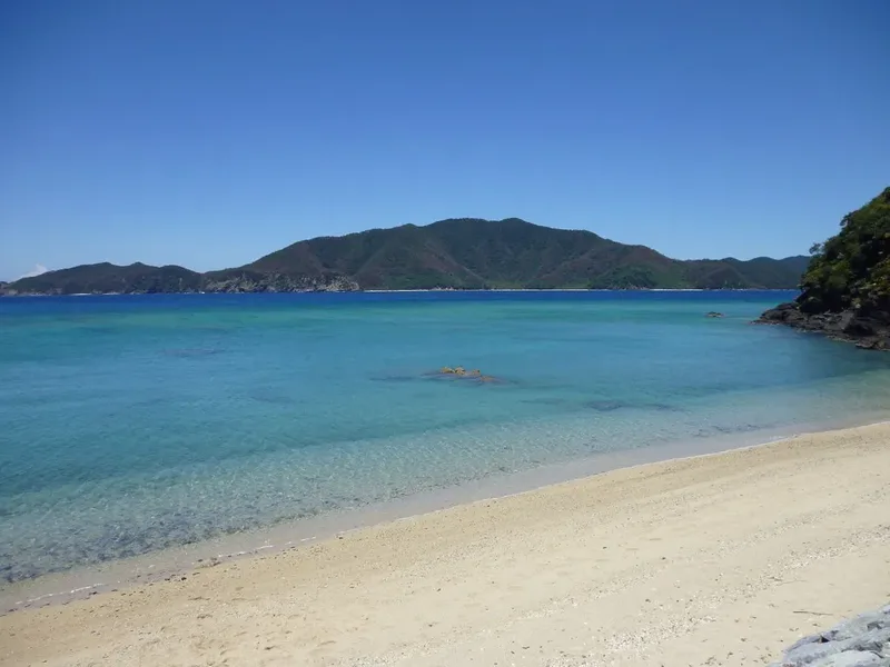 Clear coastal water, sand and green hills on Amami Oshima.