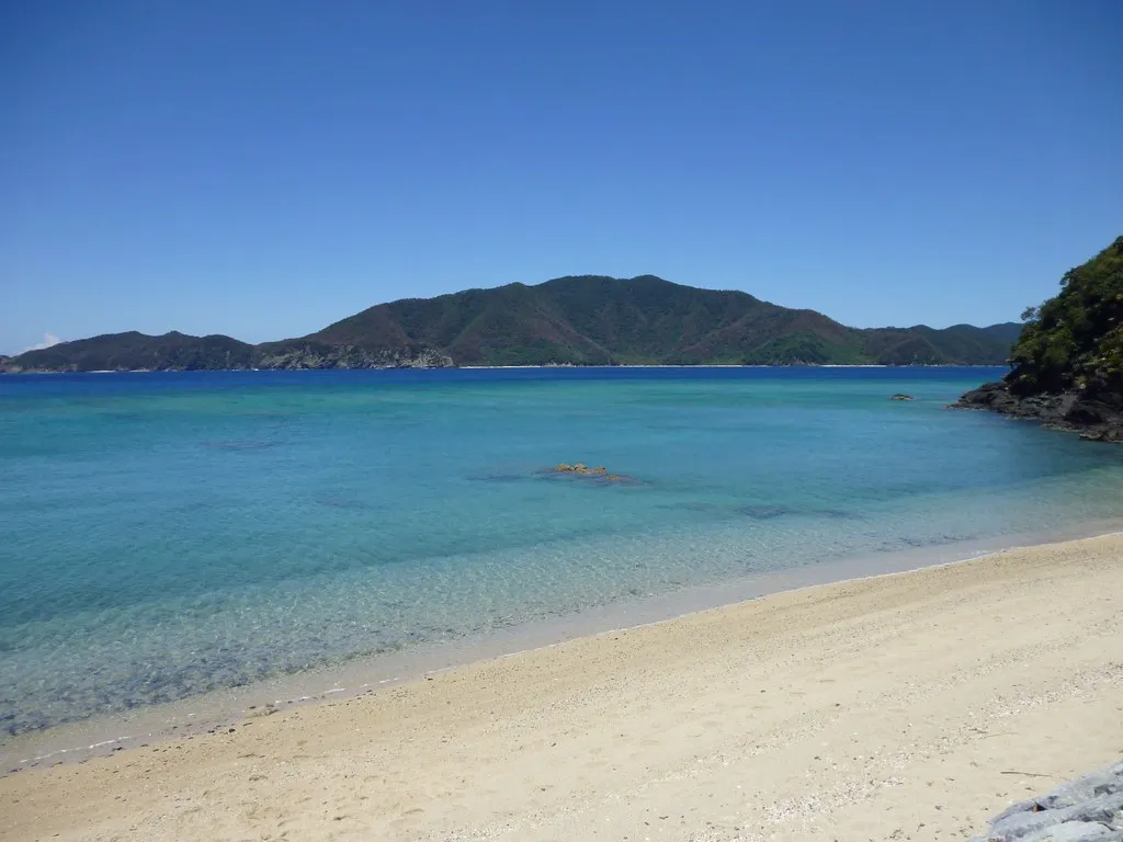 Čistá pobřežní voda, písek a zelené kopce na Amami Oshima.