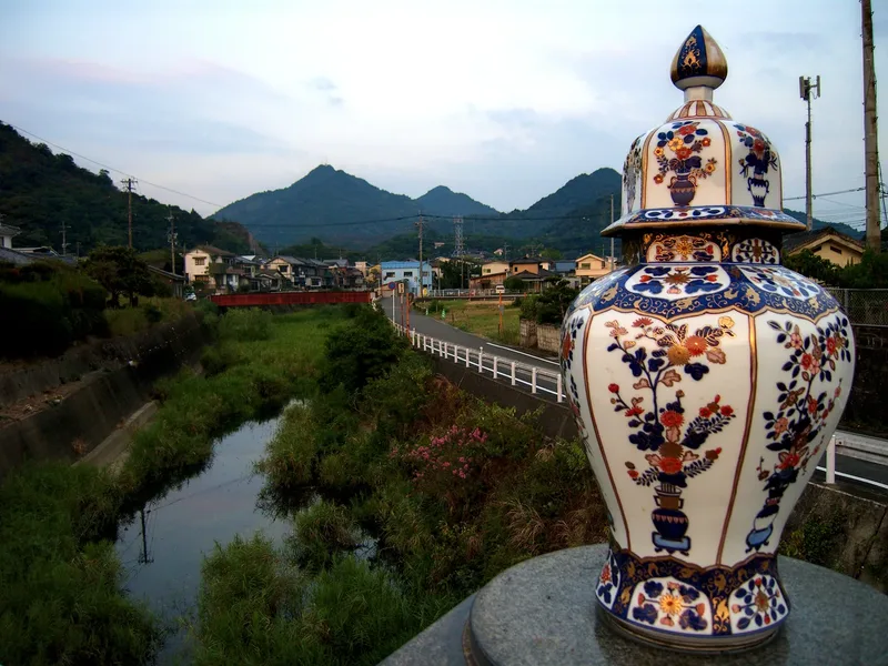 A decorative porcelain vase on a bridge in Arita, with river and mountains beyond.