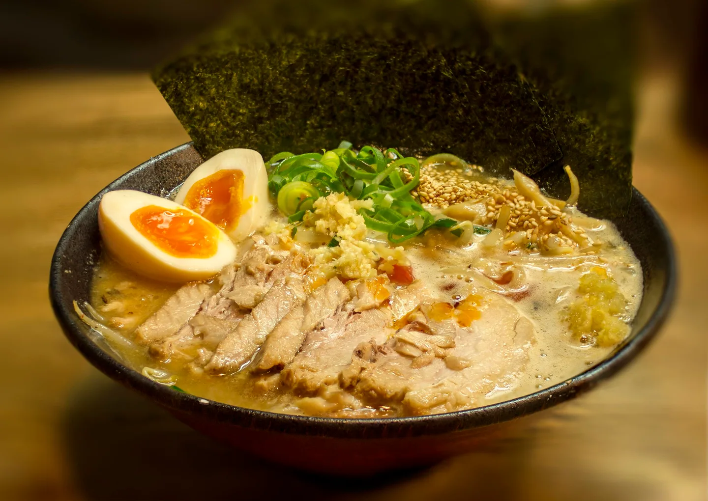 Miso ramen with pork, egg, spring onion and nori in a dark bowl.