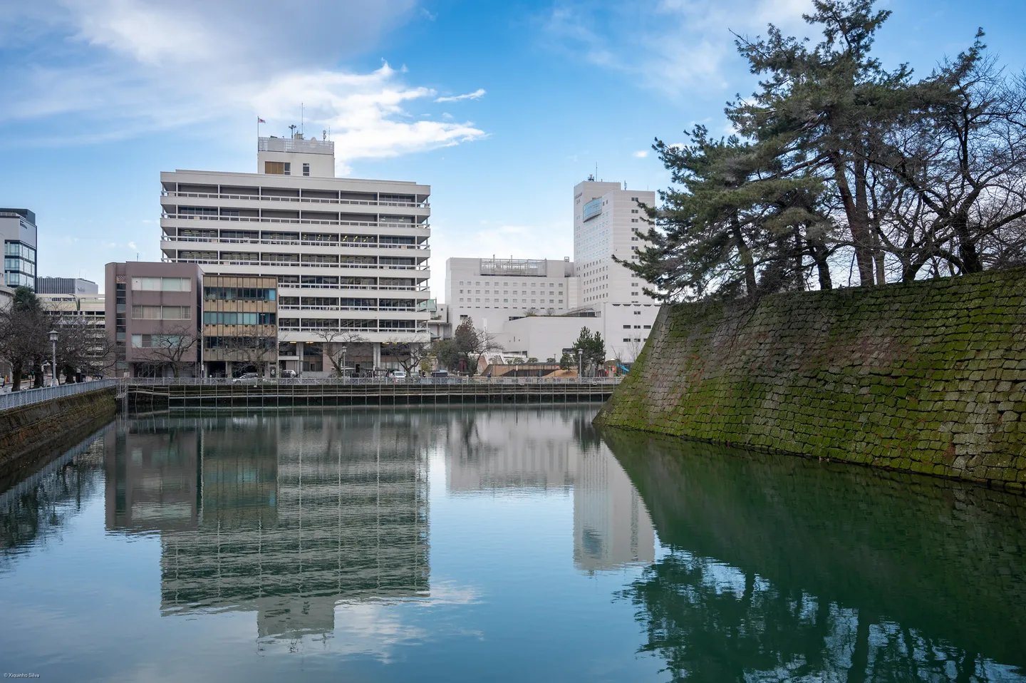Acqua, mura di pietra ed edifici moderni intorno al castello di Fukui.