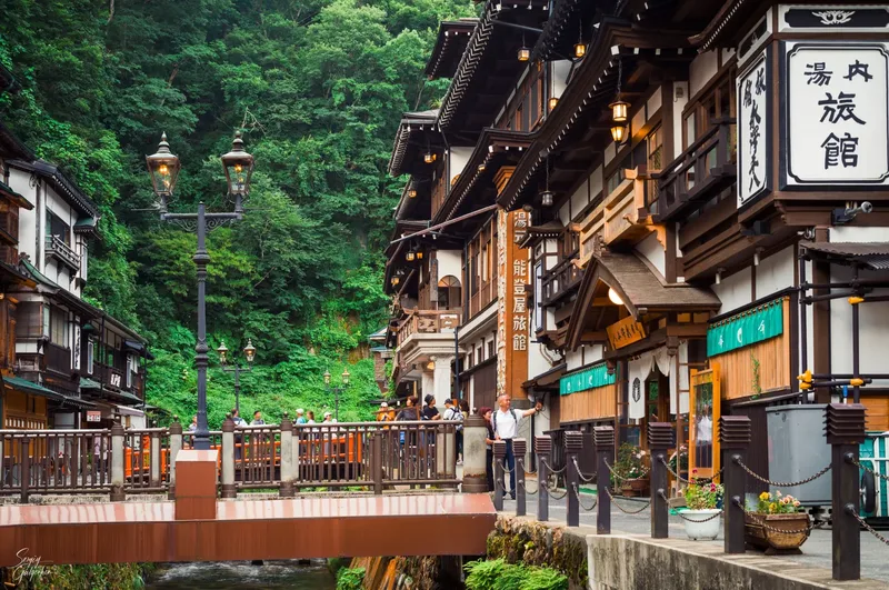 Traditional riverside buildings, a bridge and green trees in Ginzan Onsen.