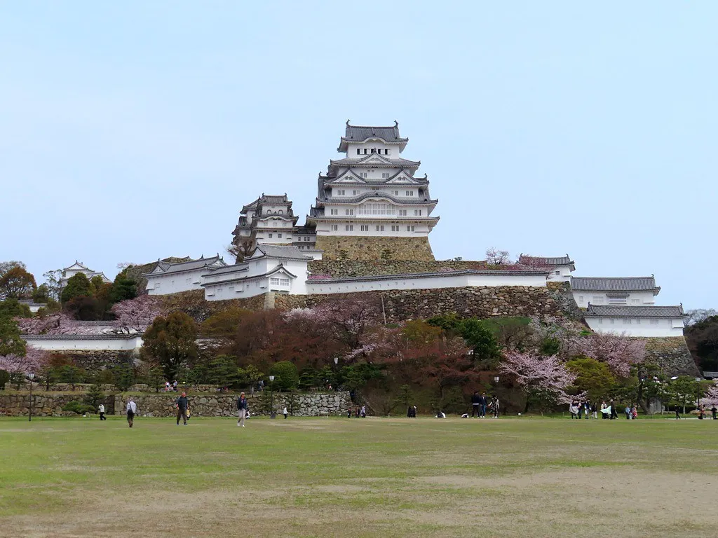 Bílá pevnost hradu Himeji nad kamennými zdmi a stromy.