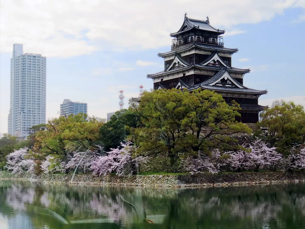 Castelul Hiroshima deasupra șanțului său, încadrat de flori de cireș.