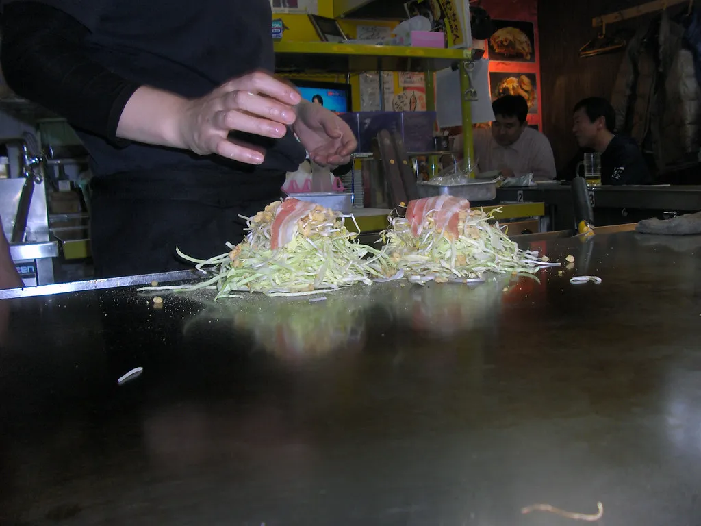 Okonomiyaki în stil Hiroshima, pregătit în straturi pe o tavă.