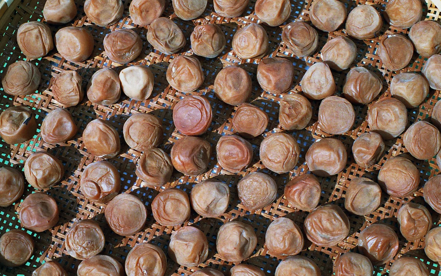 Umeboshi-plommer arrangert på en vevd overflate for tørking.