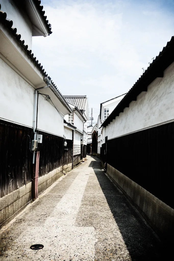 A paved lane between white storehouses in Kurashiki's Bikan district.