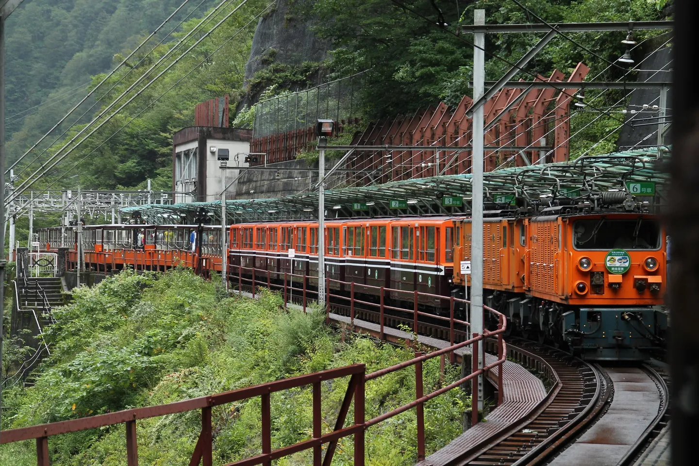 Kurobe Gorge Eisenbahn Zug auf einer Kurve zwischen Vegetation und Eisenbahnstrukturen.