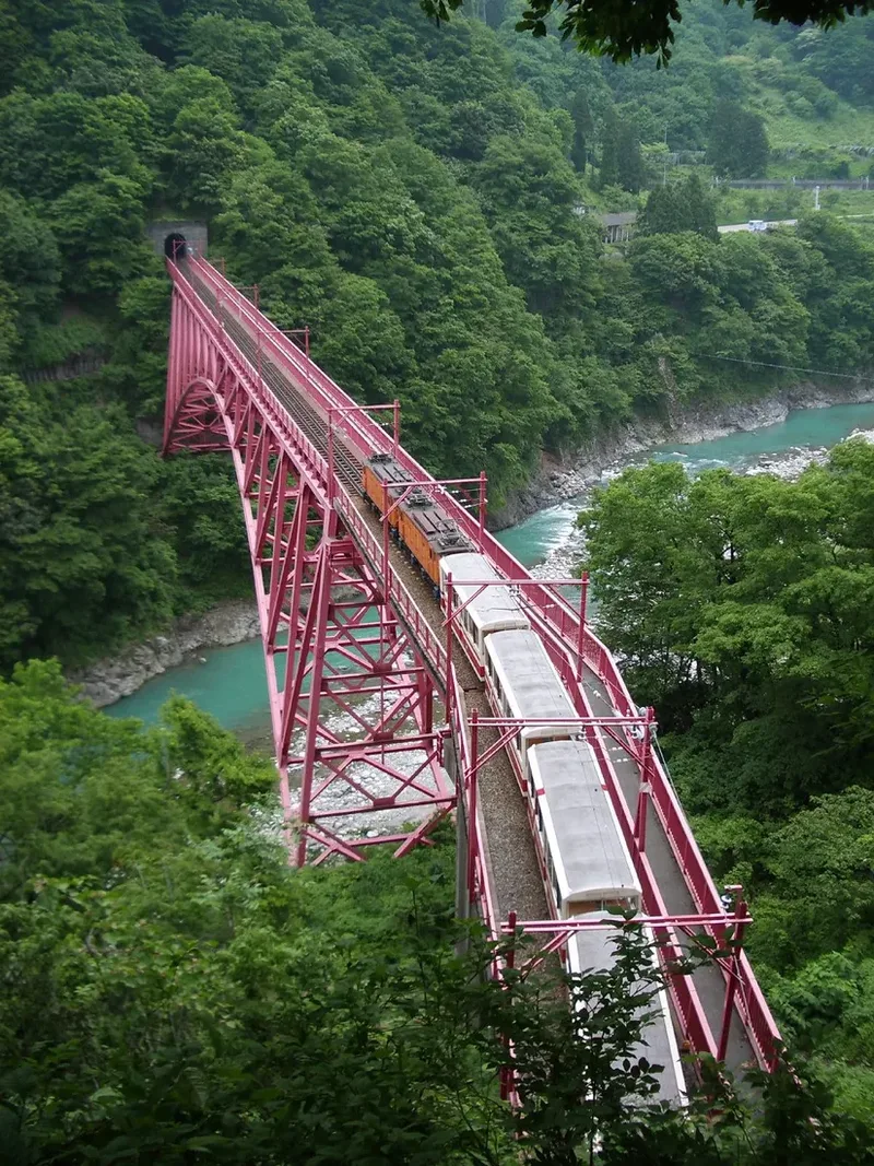 A red railway bridge between the wooded slopes of Kurobe Gorge.