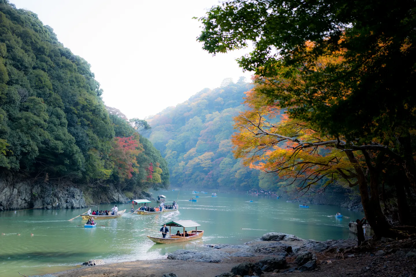 Lodě na řece mezi zalesněnými kopci v Arashiyama, Kjóto.