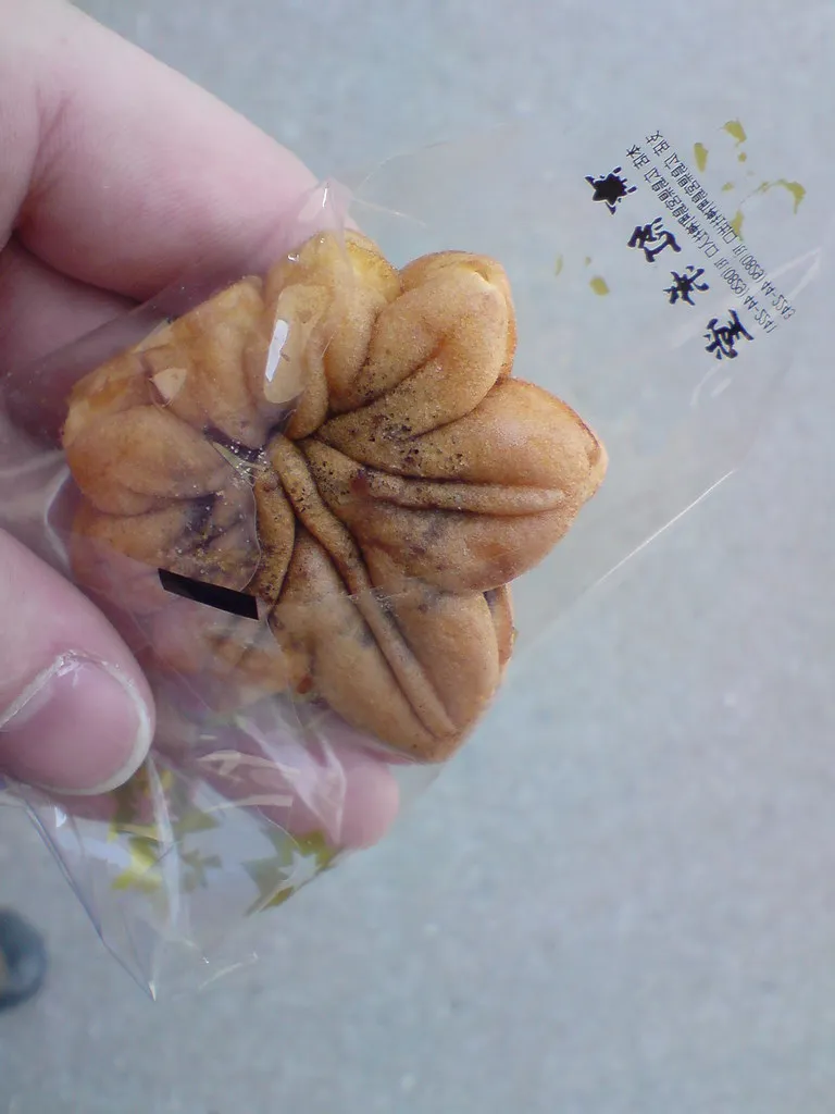 Un momiji manju în formă de frunză de arțar ținut în fața ambalajului său.