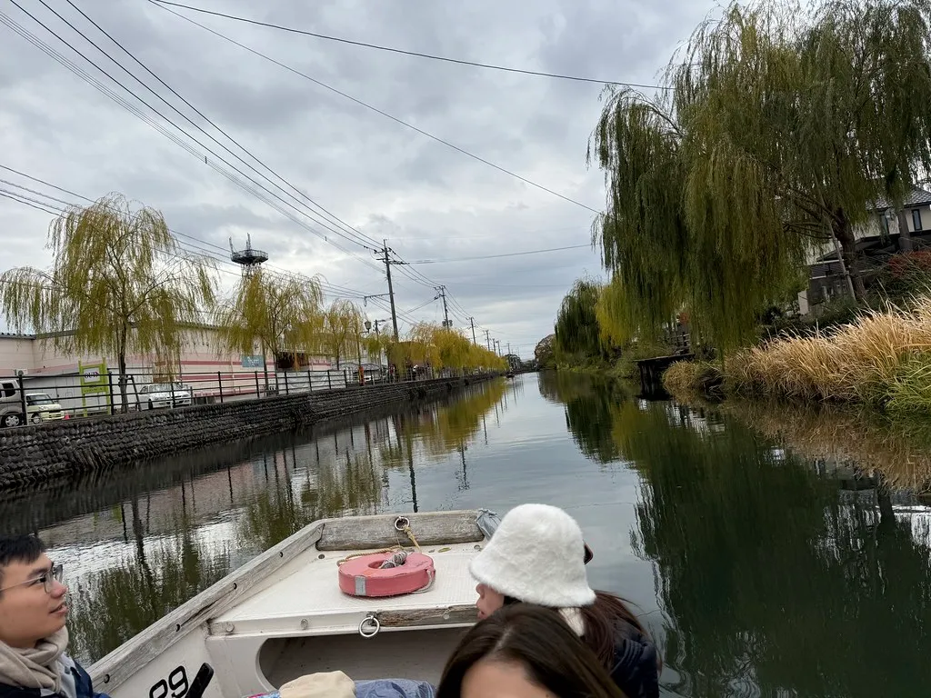 Un barco que viaja a lo largo de un canal rodeado de casas y sauces en Yanagawa.